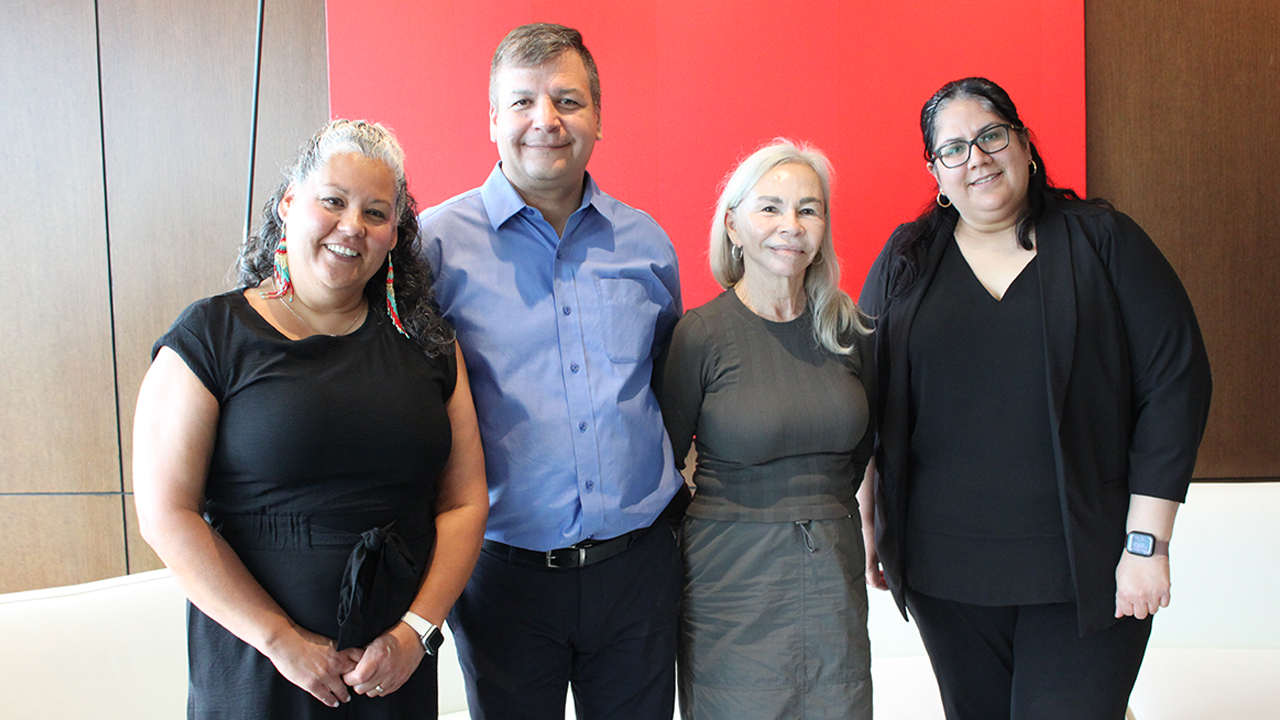 Four people stand together, smiling.