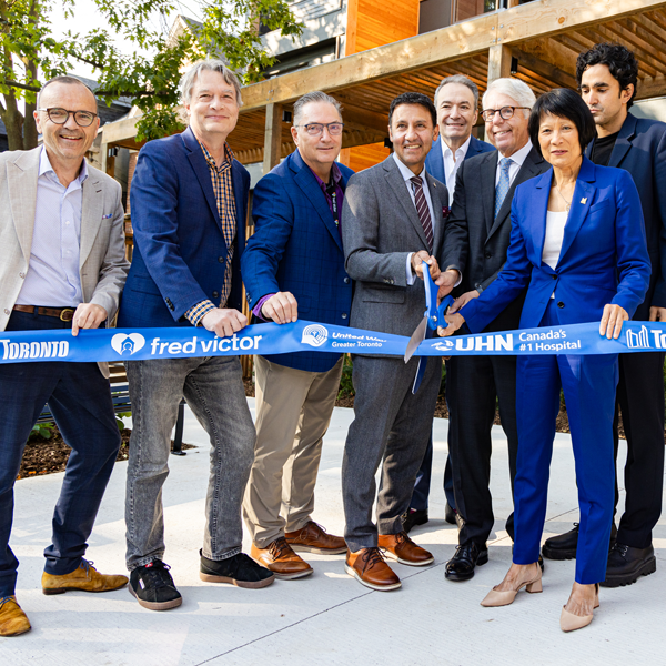 A picture of eight people in suits cutting a blue ribbon to celebrate the opening of the Social Medicine Initiative supportive housing.