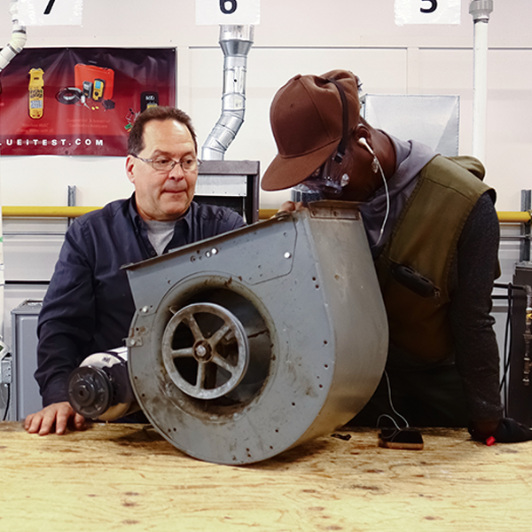 A group of people standing around a man sawing a piece of wood.