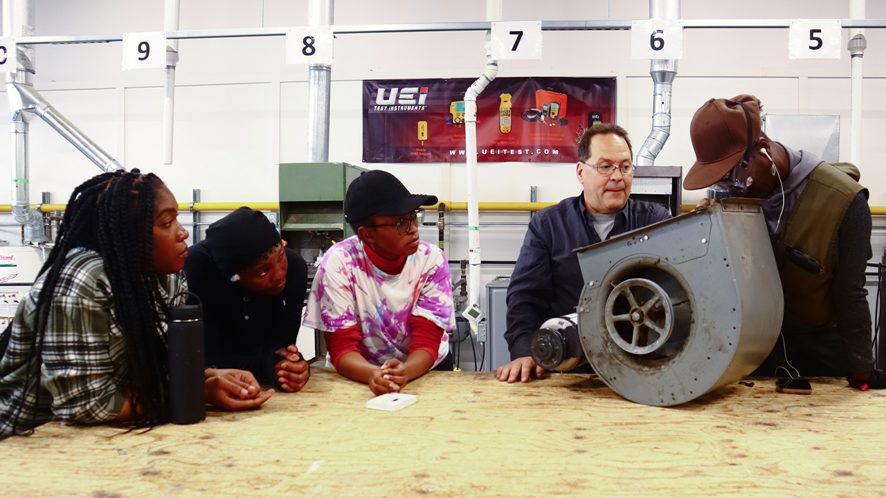 A group of people standing around a man sawing a piece of wood.