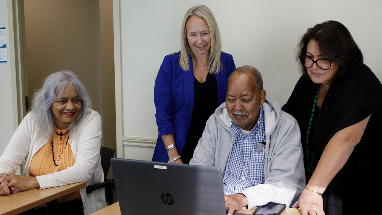 A group of four people gather around a laptop.