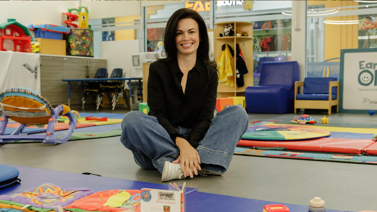 Michelle Dagnino, the executive director of the Jane/Finch Centre, sits on the floor of a playroom and smiles at the camera.