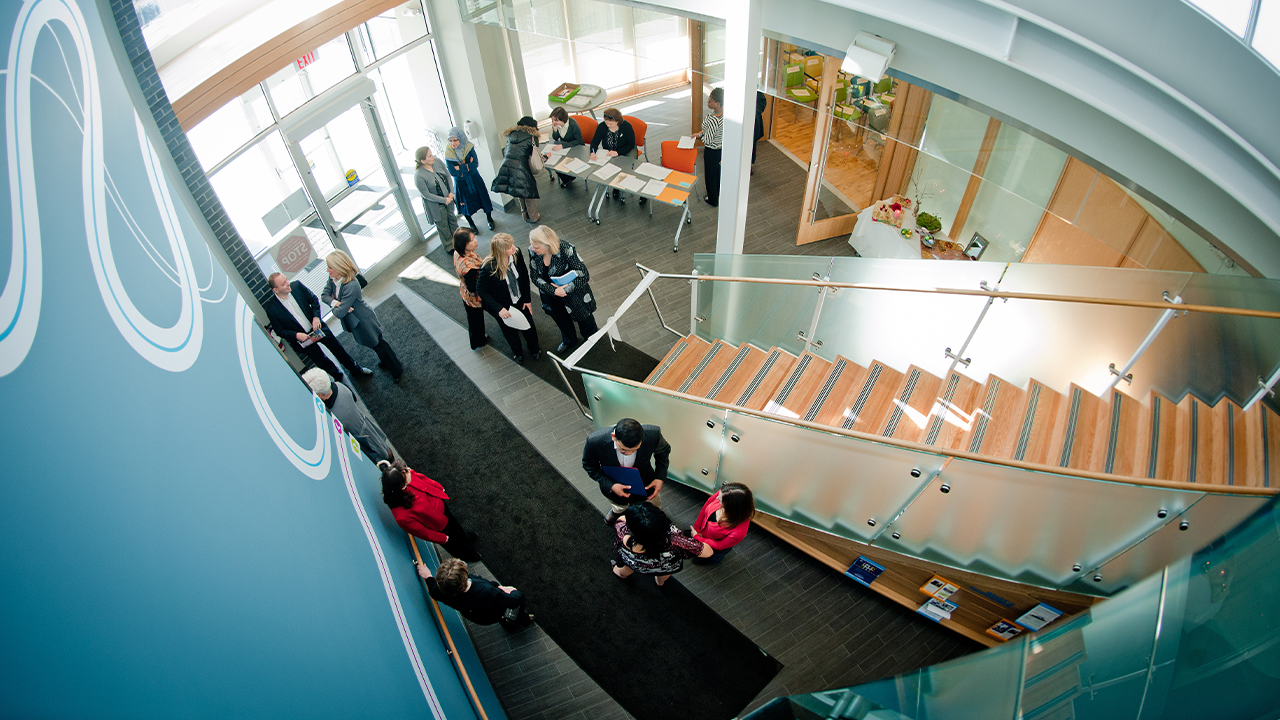 The entrance of the Bathurst Finch Hub filled with people talking in small groups, taken from the second floor looking down. 