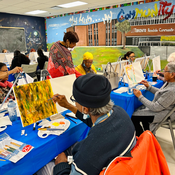 People painting in a room with a wall mural that says ‘Rexdale Community Hub’.