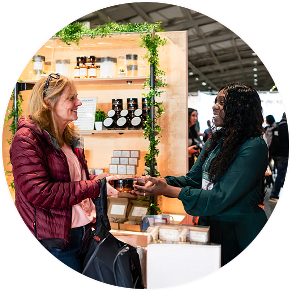  A Black woman, one of the Inclusive Local Economic Opportunity (ILEO) initiative Storefront Starter program entrepreneurs, speaks with a customer at a booth featuring her products. 